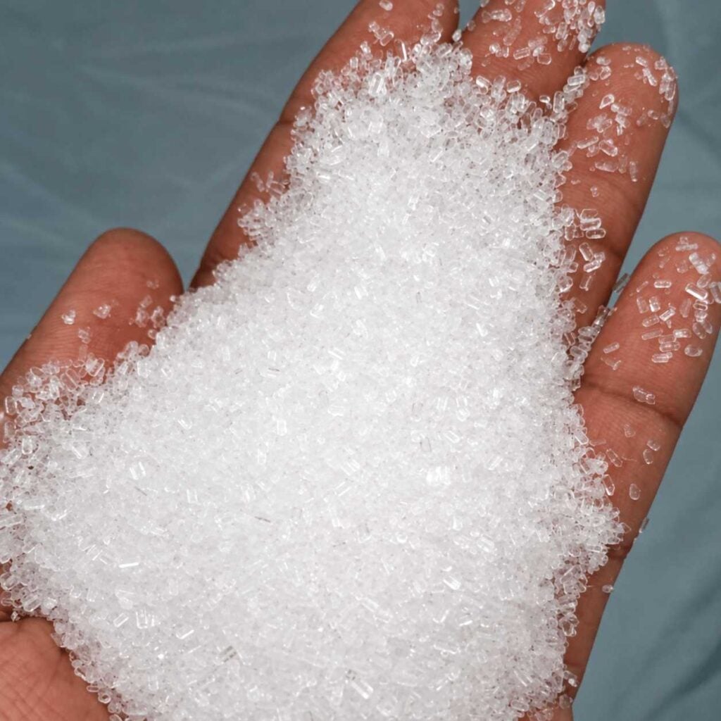 Epsom salt crystals: Close-up of a hand holding a mound of coarse white Epsom salt crystals.